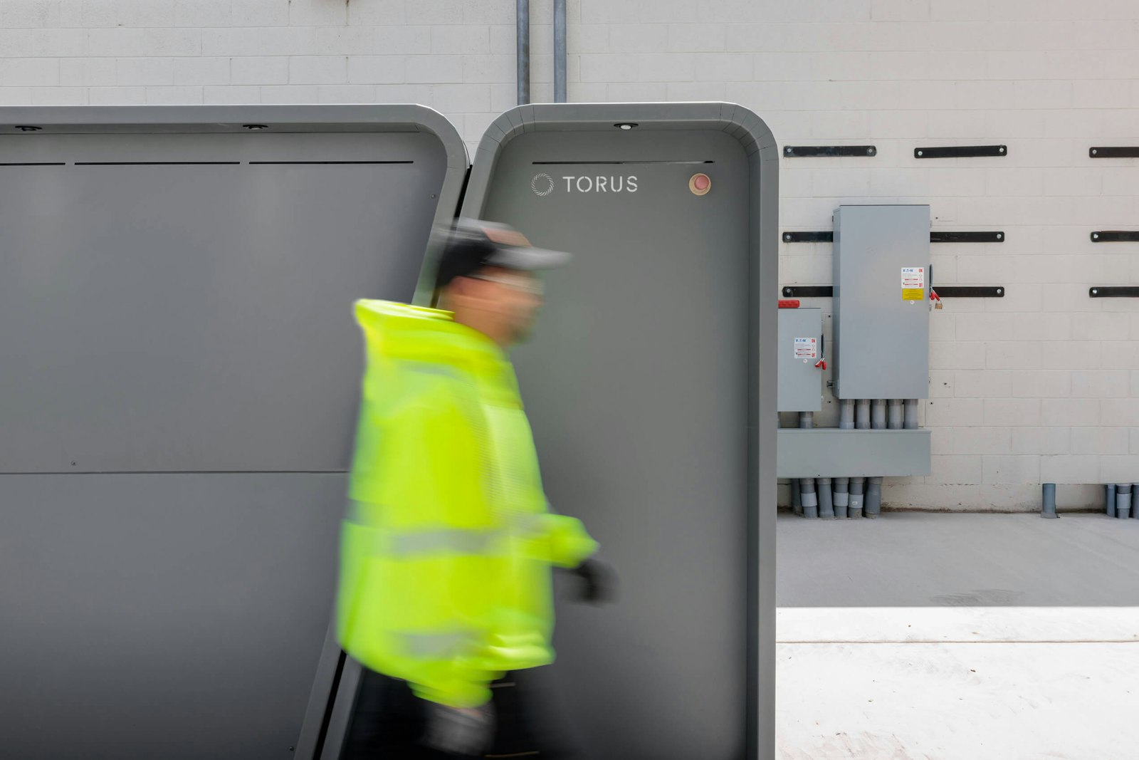 A worker in a bright safety jacket passes installed Torus energy cabinets