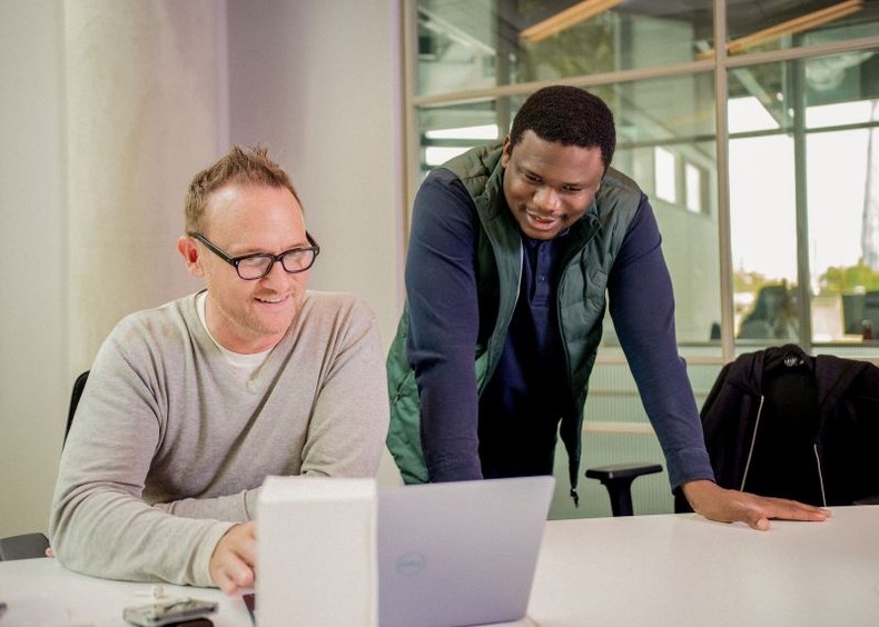 Tosin Eniolorunda leaning over a laptop while working with a colleague