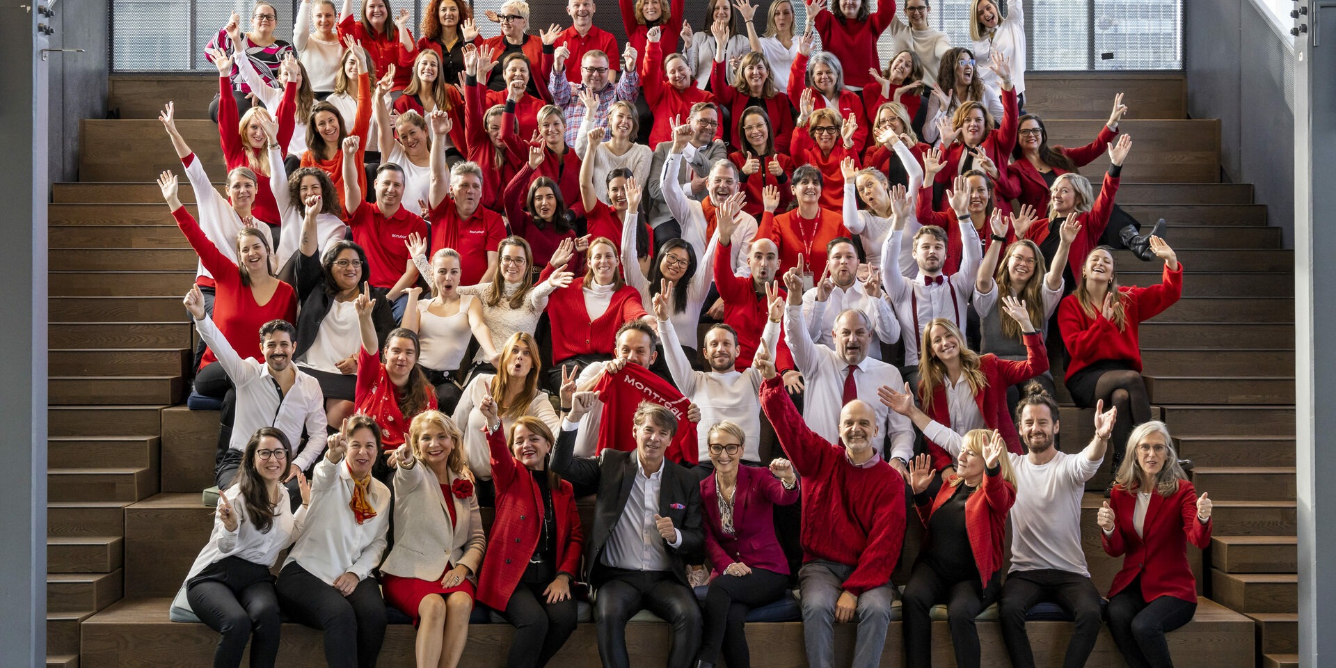 Tourisme Montréal staff gathered on broad wooden steps, wearing red, white and black and waving at the camera
