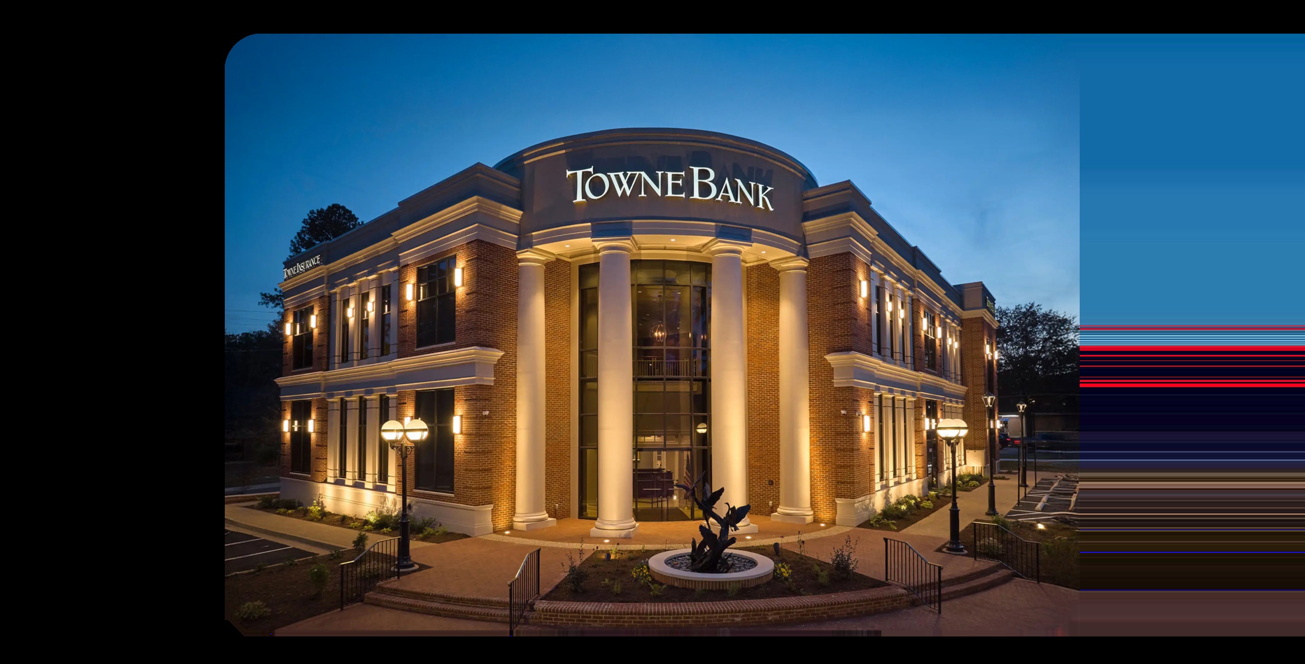 TowneBank building illuminated at dusk, with columns and a sculpture outside