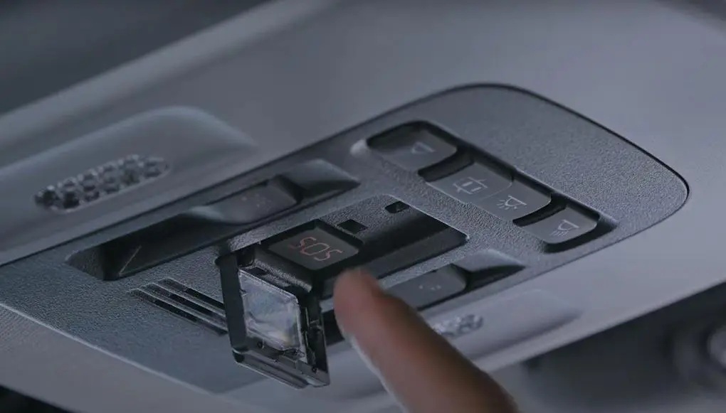 A finger presses the red SOS button in a Toyota overhead console