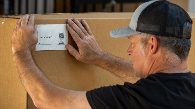 A worker applies a Trackonomy SmartTape label to a cardboard shipping box
