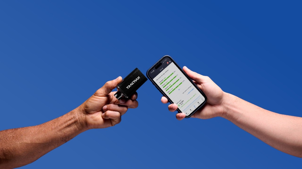 Hands holding a Tractian wireless sensor and a phone displaying machine information