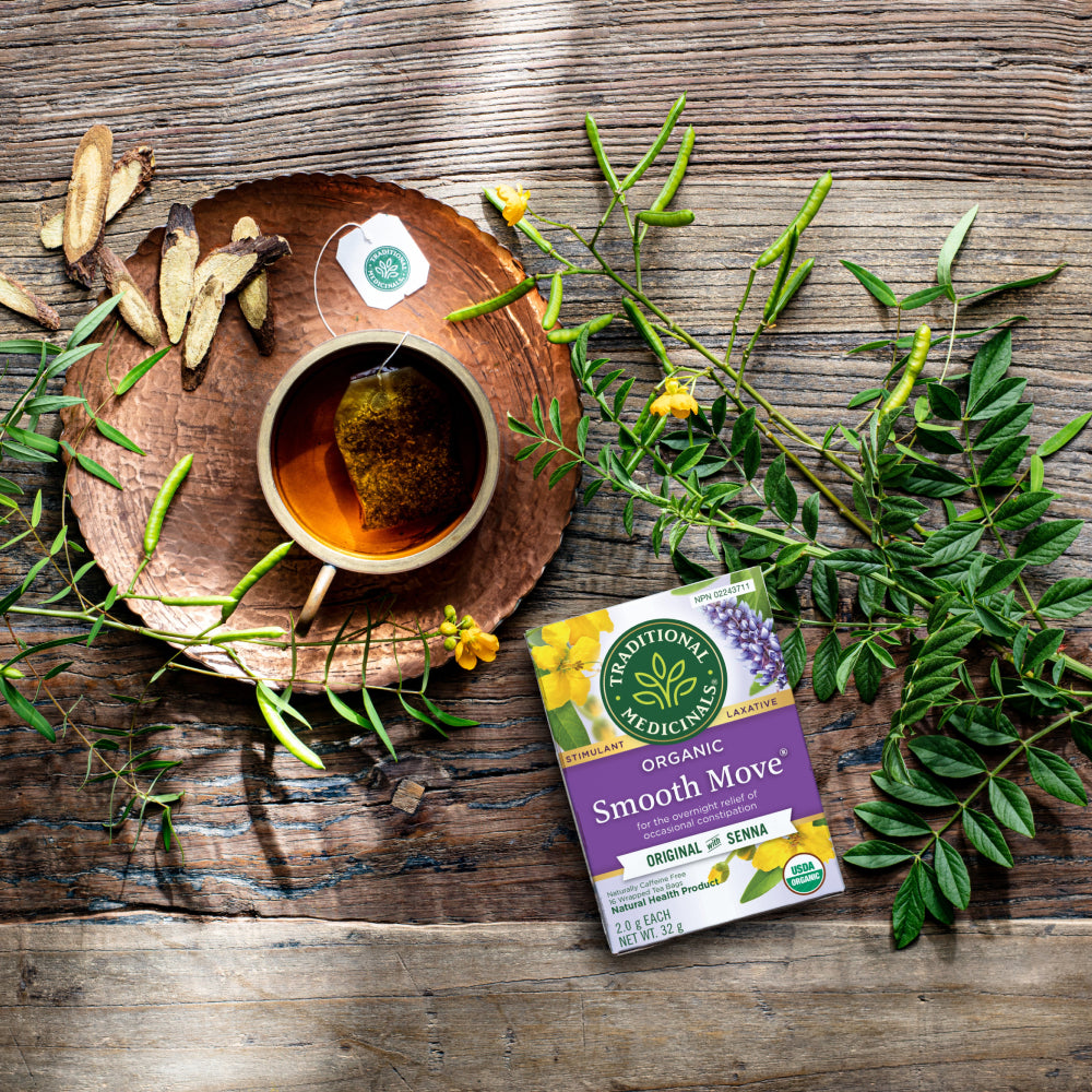 Smooth Move tea box beside a cup, herbs and roots on a wooden table