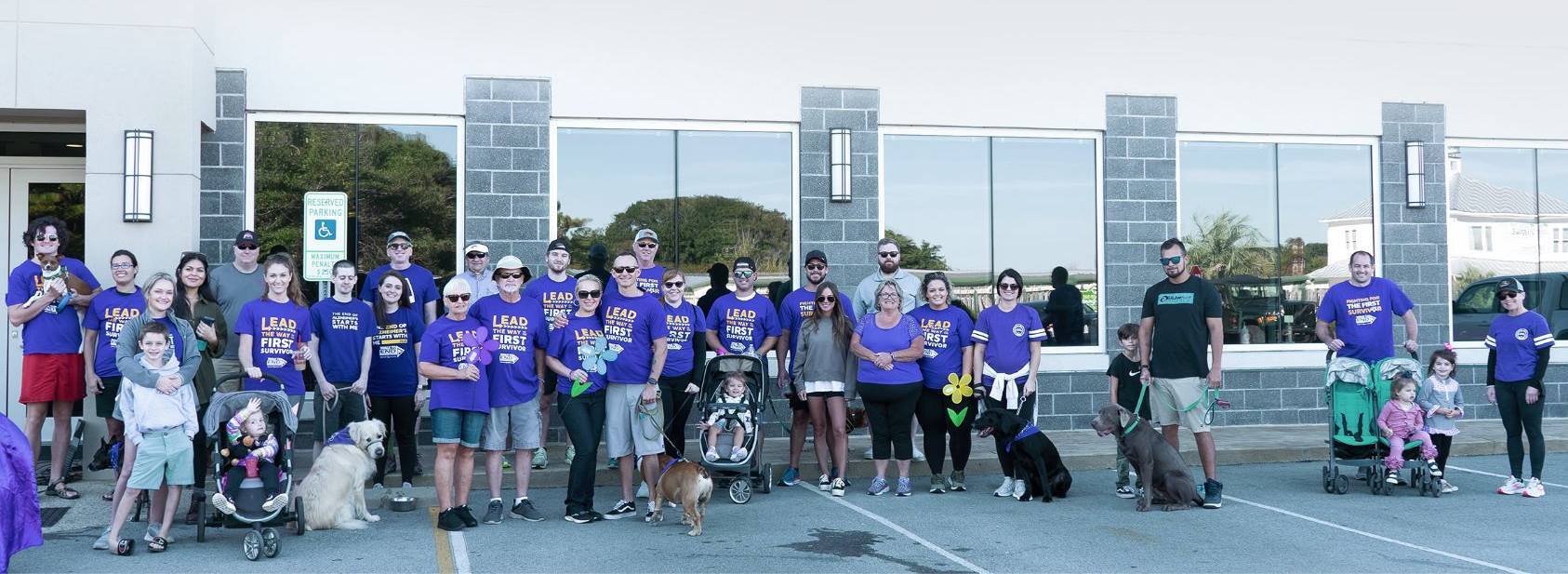 TransImpact IMPACT1 participants gathered outdoors in purple Walk to End Alzheimer’s shirts with families and dogs