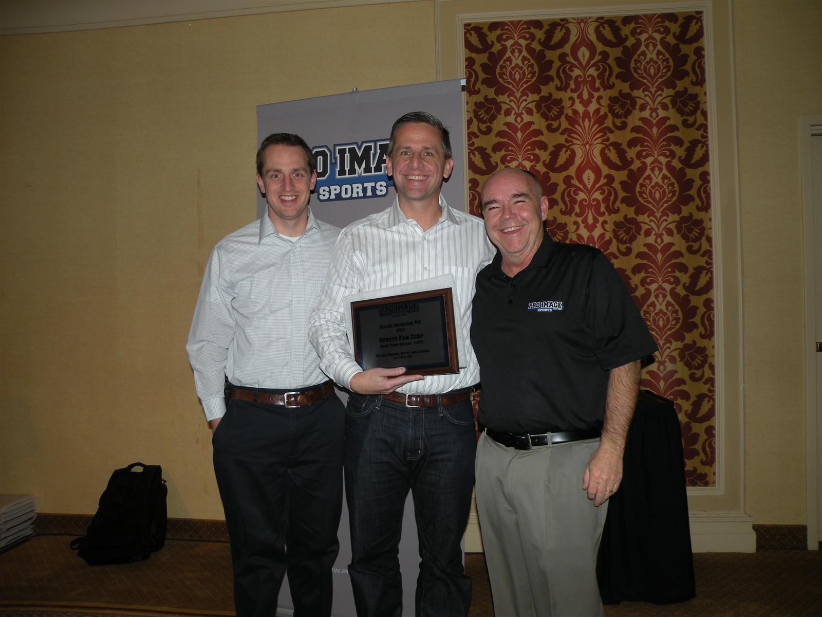 Travis Hawkes with Pro Image Sports CEO Dave Riley and Sports Fan Corp executive Brandon Miner at a retail award presentation