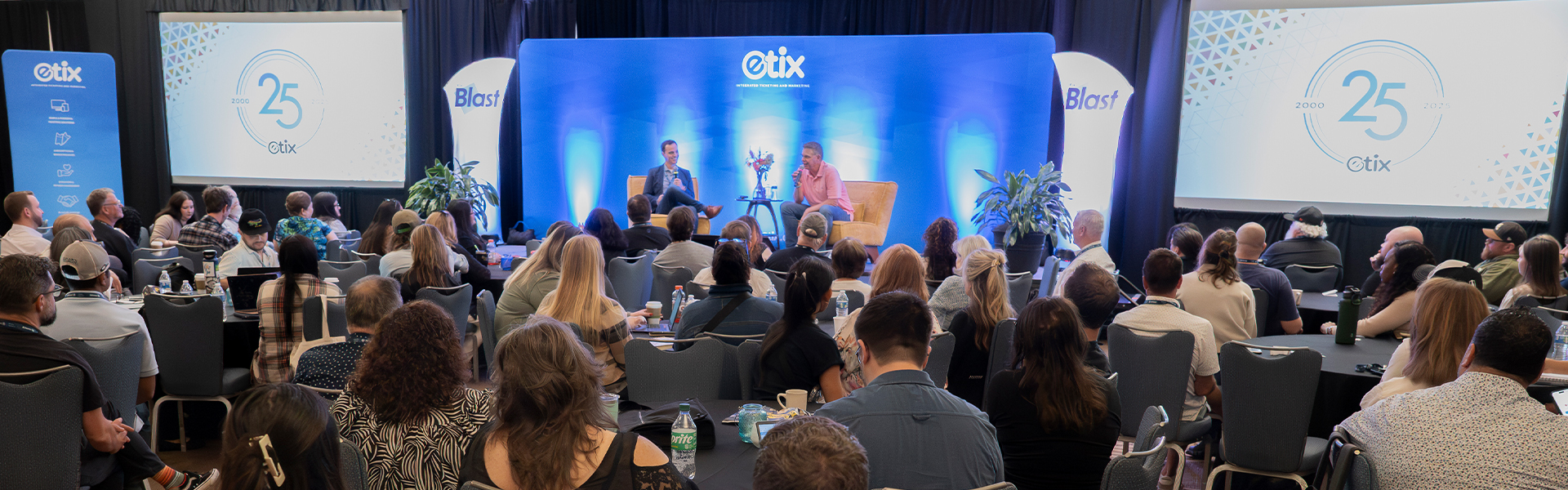 An Etix Blast audience watching two speakers in conversation on a blue-lit stage.