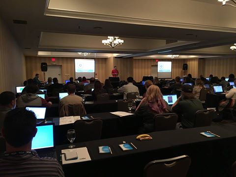 Travis Janovich addressing an Etix Live training room, with attendees working on laptops.