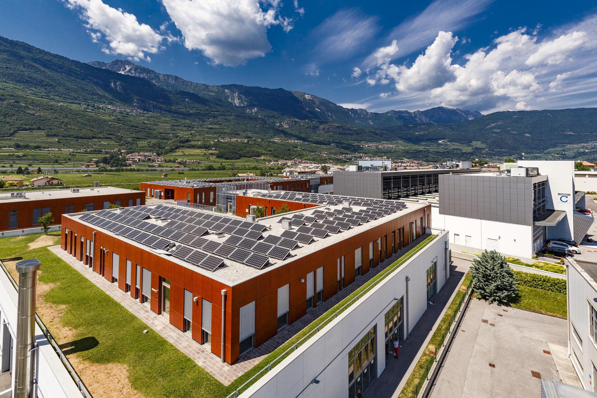 Polo Meccatronica buildings with rooftop solar panels beneath the mountains of Rovereto