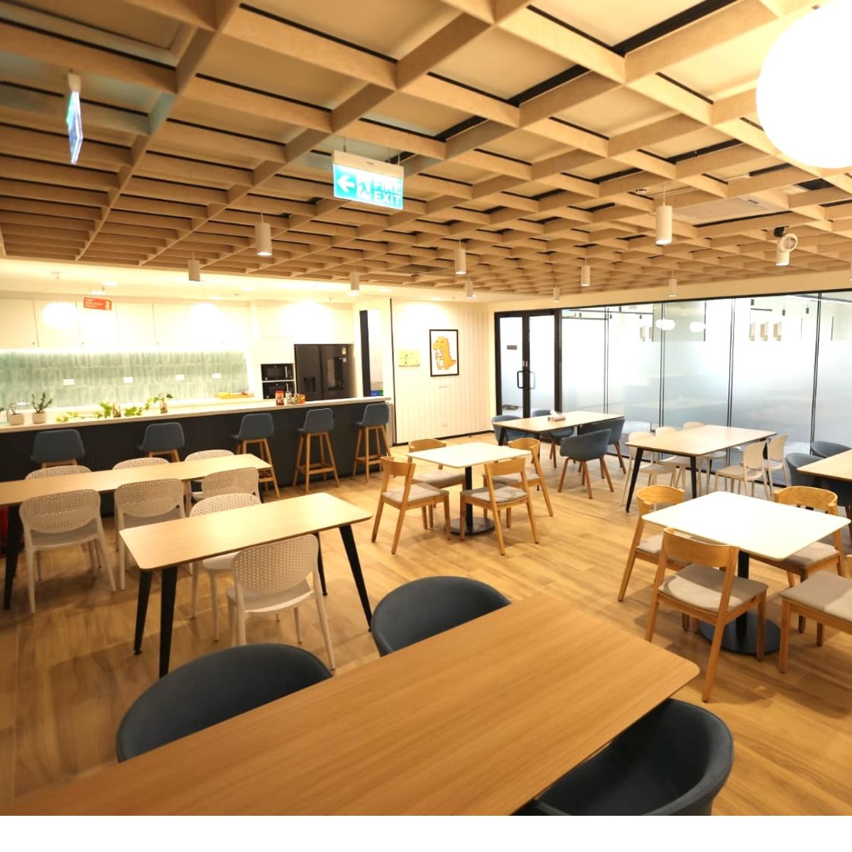 Tables and shared seating beneath a timber-patterned ceiling in Trexquant’s new India office