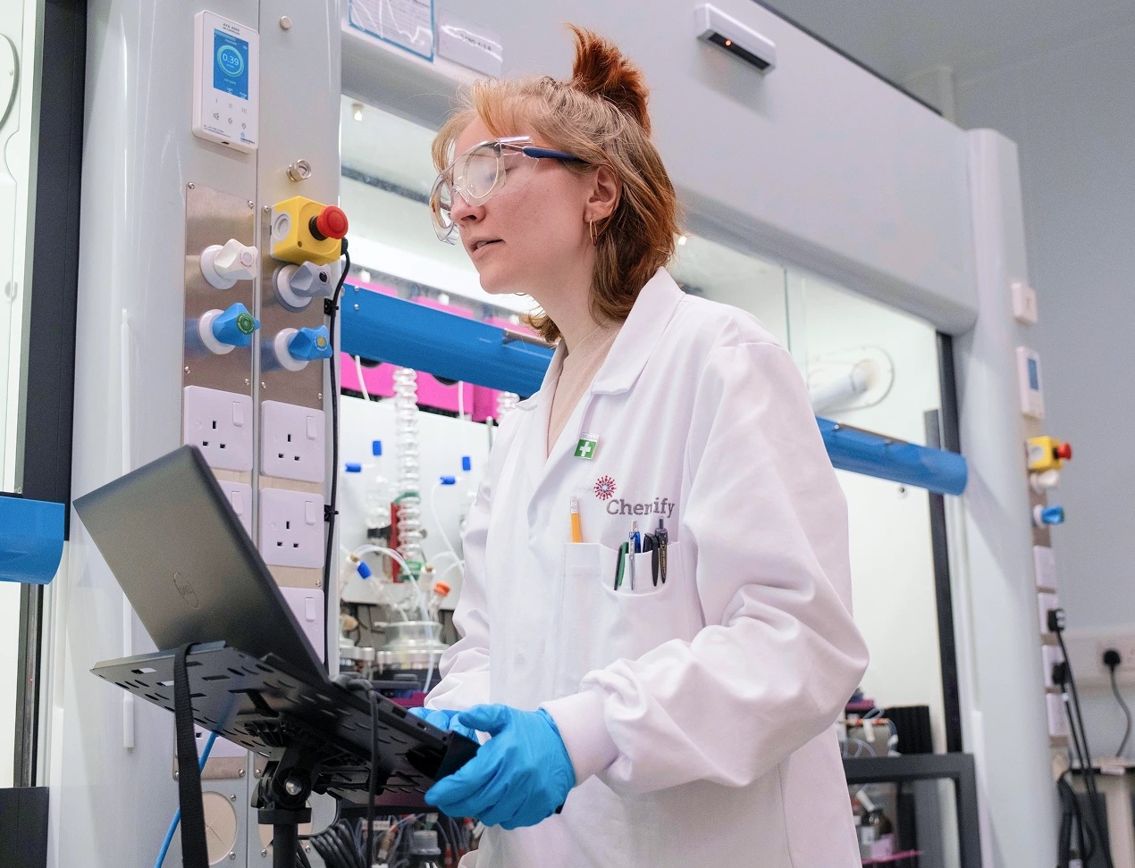 A Chemify scientist uses a laptop beside robotic chemistry equipment