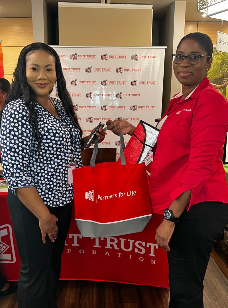 A UTC representative and attendee with a red Partners for Life bag at UDECOTT’s 2024 Financial Fair