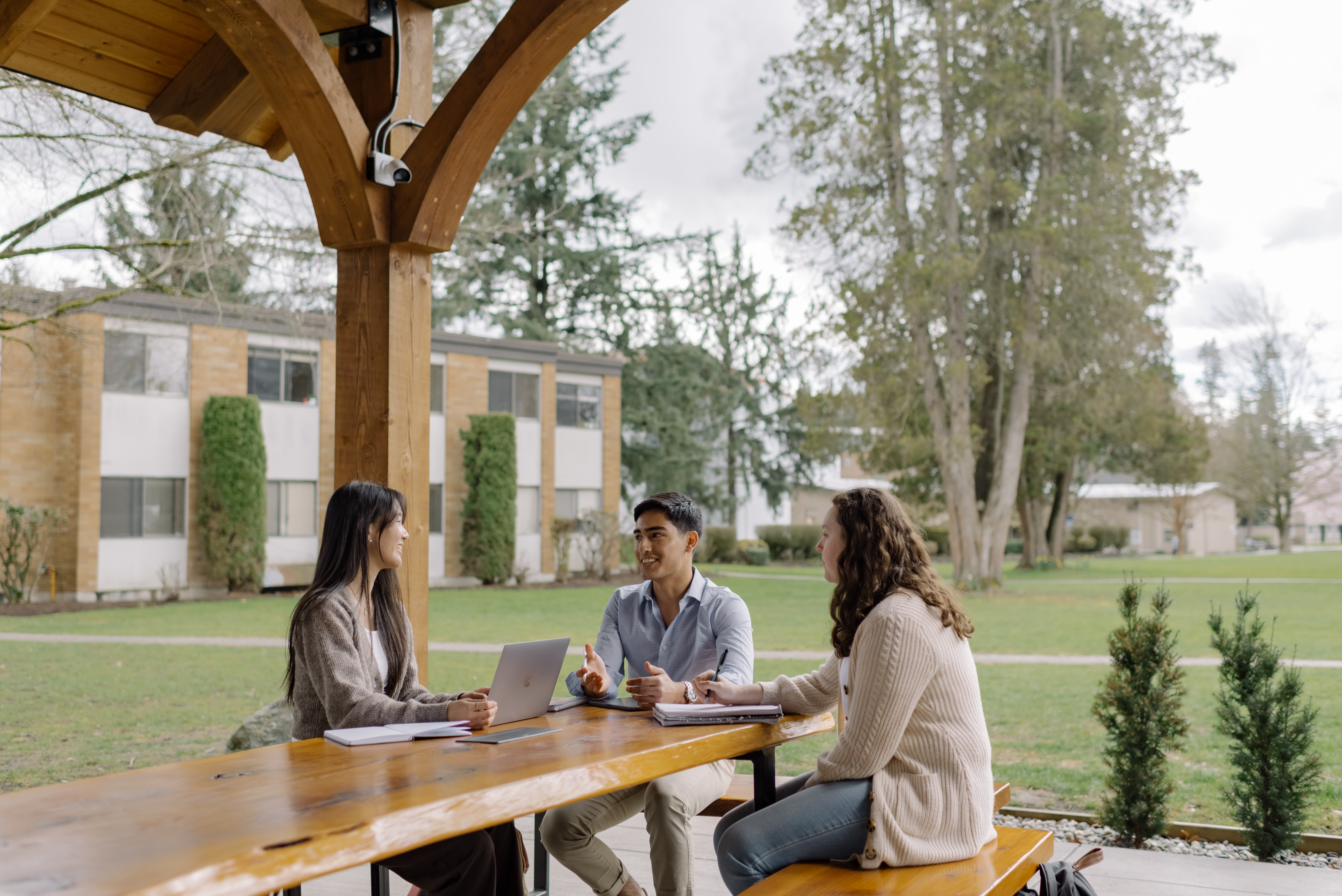 Three Trinity Western students talk around a table on the Langley campus