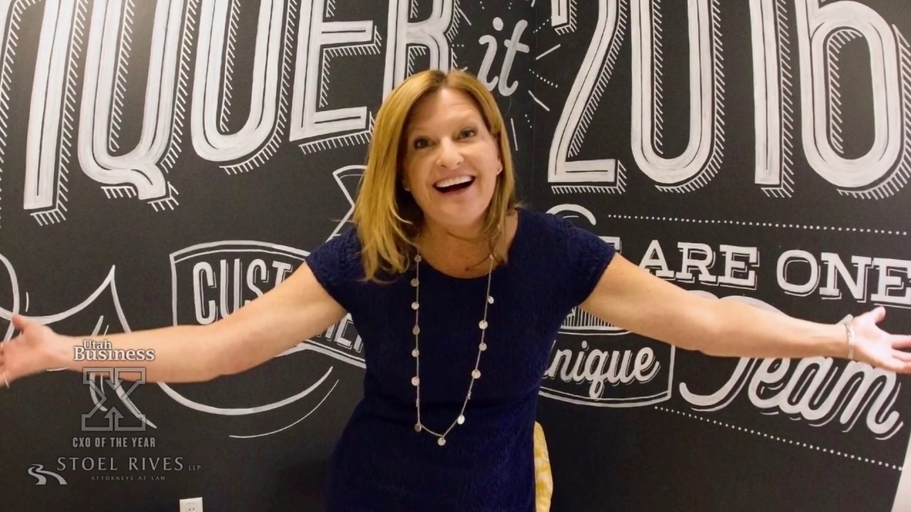 Trish Stromberg smiling with her arms outstretched in front of a hand-lettered Qqest wall in a Utah Business CXO of the Year video