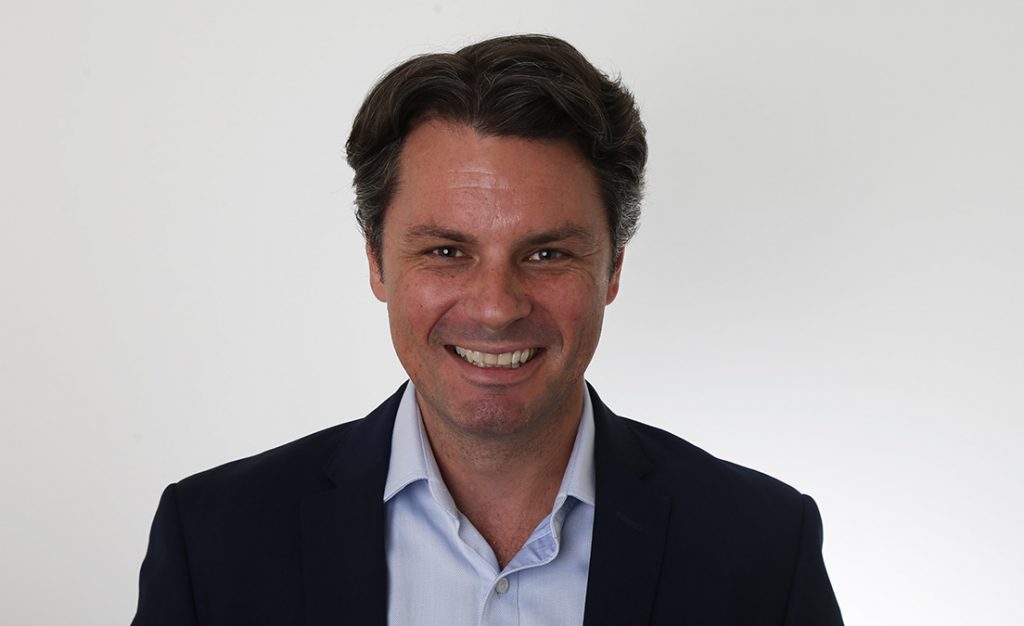 Tristan Edwards smiling in a dark jacket and pale blue shirt