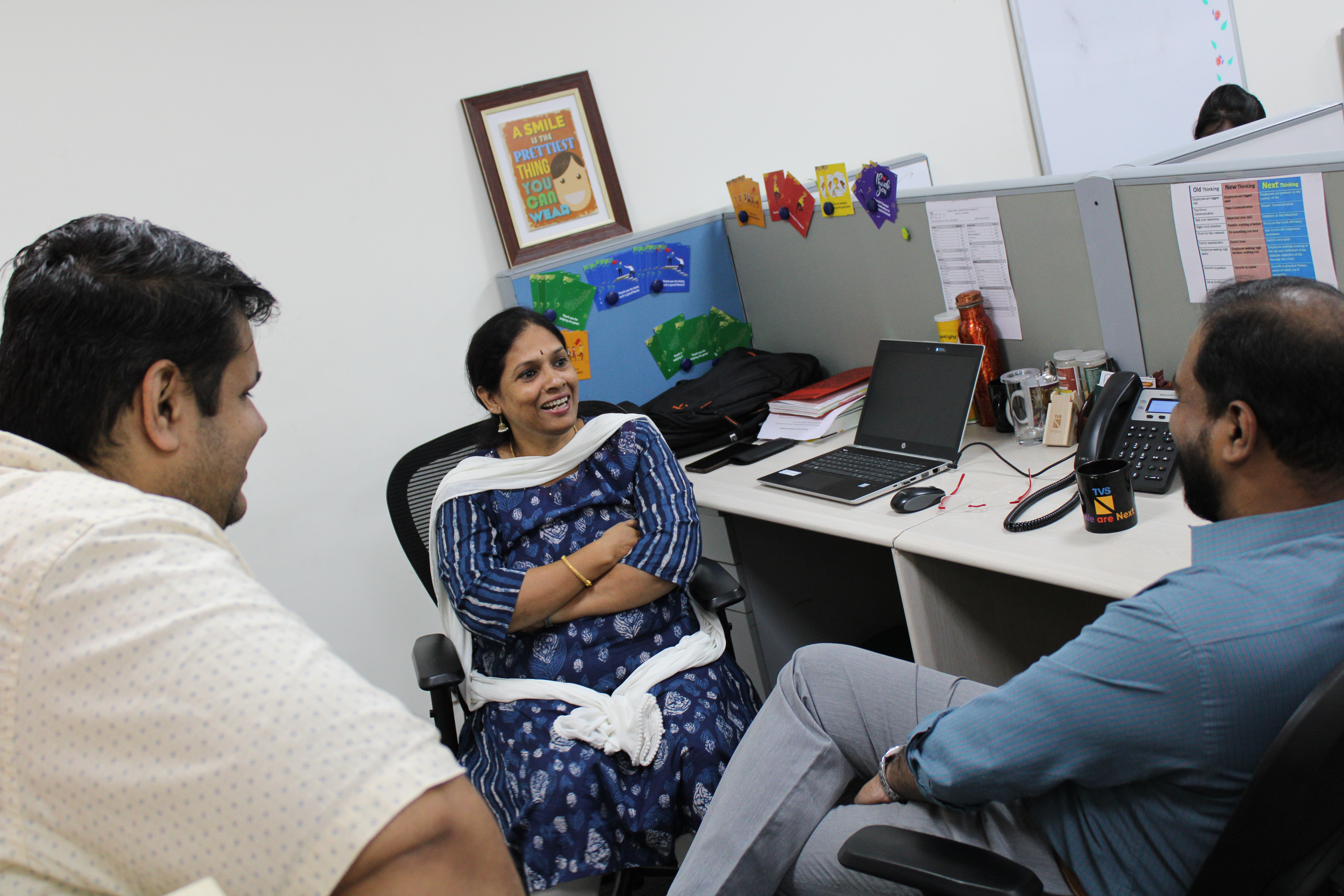 Three TVS Next colleagues talking around an office desk