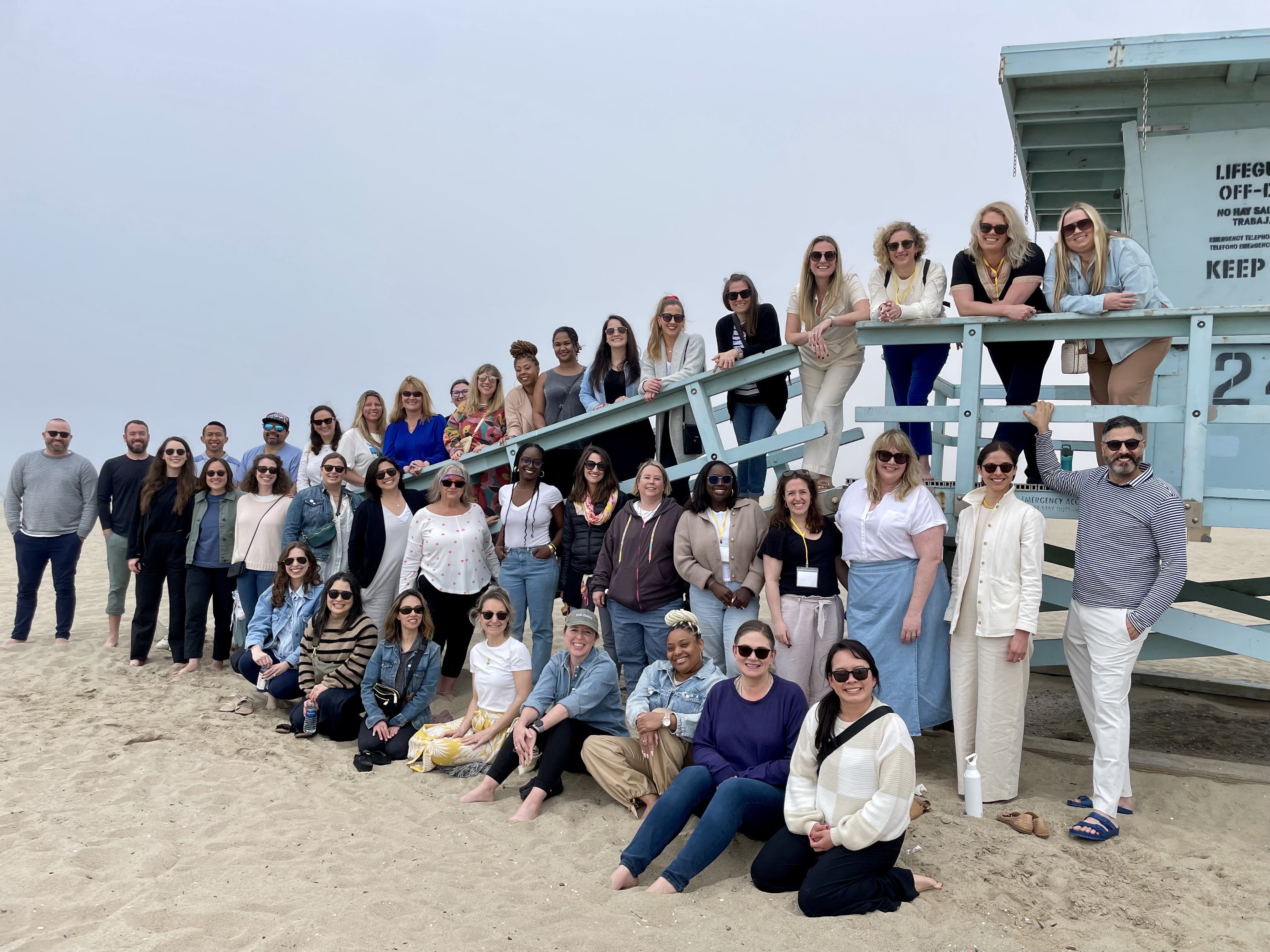 A group of Two Chairs team members gathered beside a beach lifeguard station