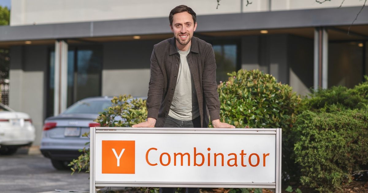 Tyler Bosmeny standing behind the Y Combinator sign outside its offices
