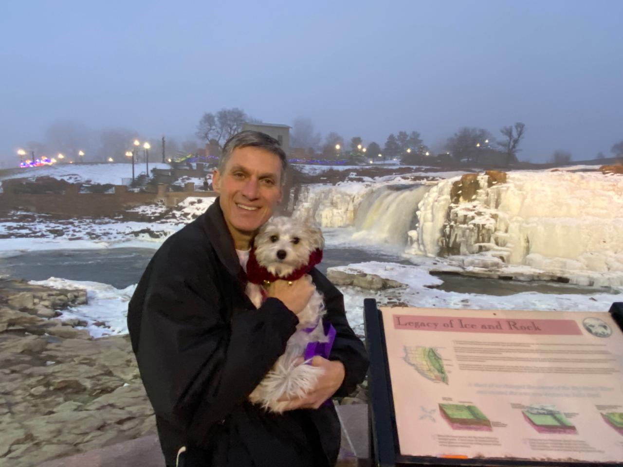 Tyler Haahr holding his rescue dog Stevie beside the snowy falls in Sioux Falls