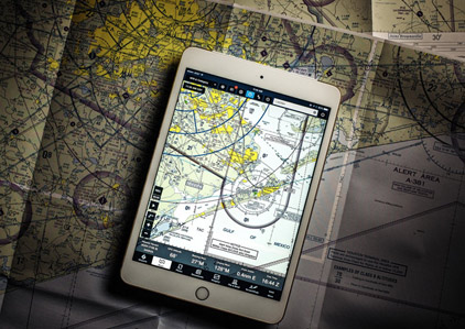 An iPad displaying ForeFlight charts rests on a paper aviation chart