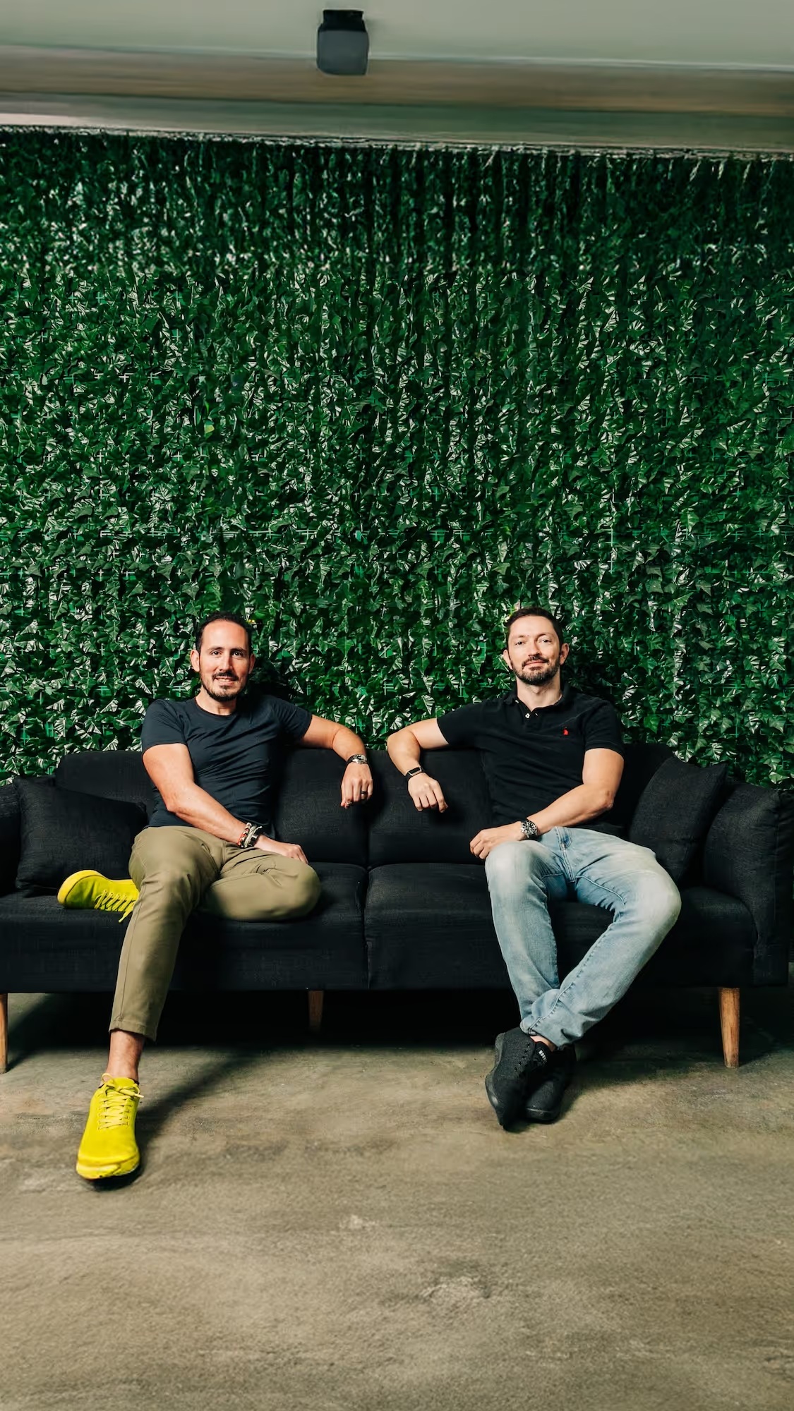 Uassist.ME co-founders seated on a couch in front of a green wall
