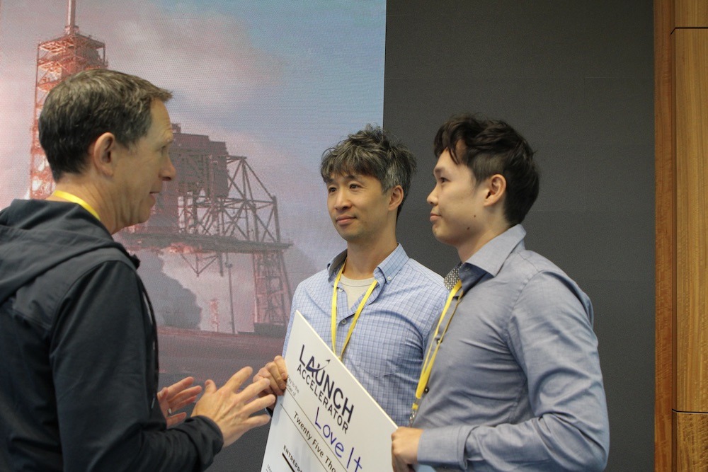 LoveIt AI co-founders Harry Jiang and Tom Lee holding their LAUNCH prize check while speaking with an attendee