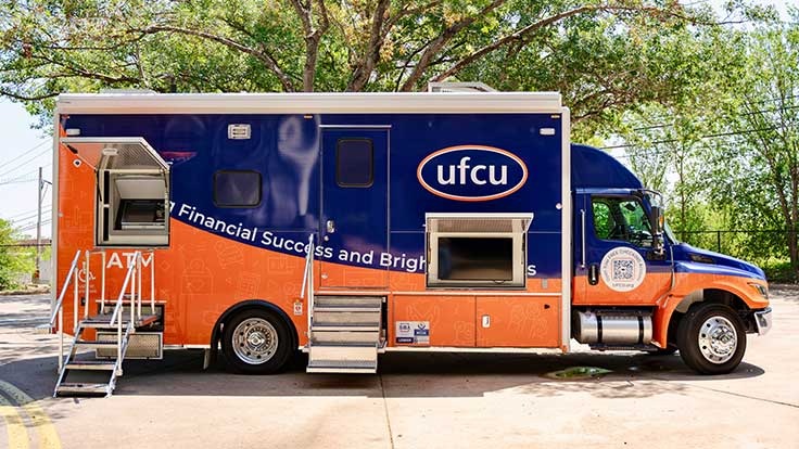 UFCU’s navy and orange mobile branch parked beneath trees, with its ATM and entrance visible