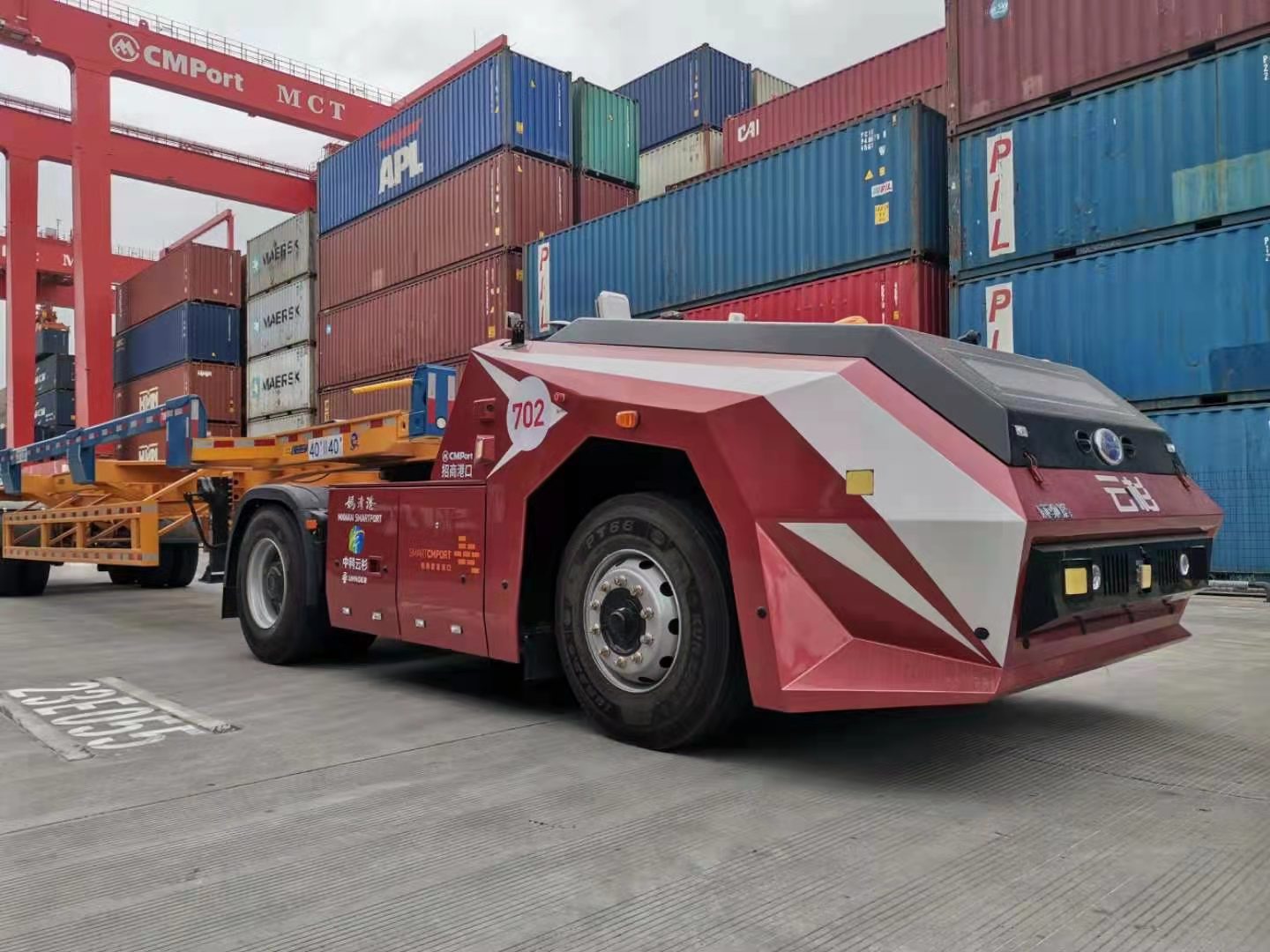 Red autonomous port truck beside stacked shipping containers at Mawan Smart Port