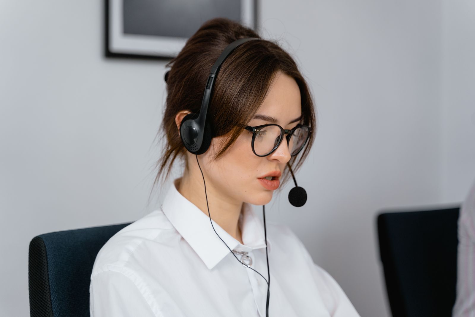 A woman wearing glasses and a headset concentrating at her desk