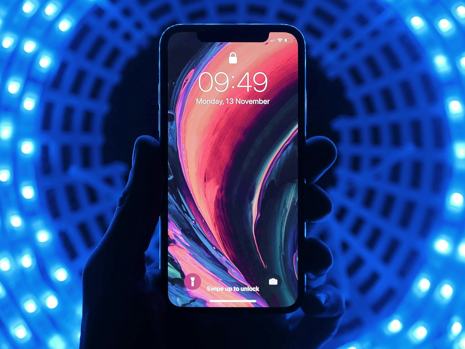 A hand holds an iPhone with a lock screen against blue lights
