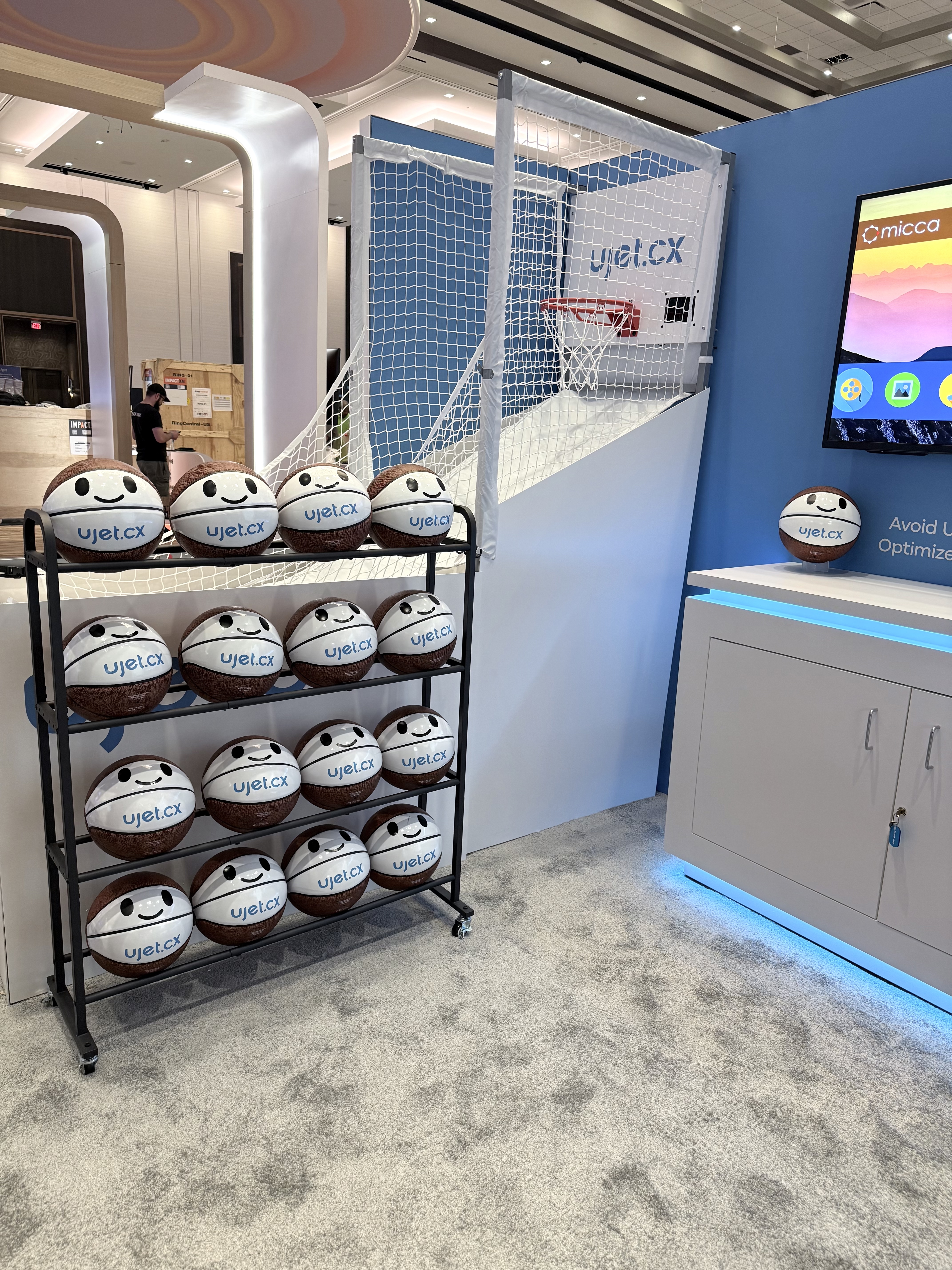 A UJET booth with a mini basketball hoop game and a tiered rack full of navy-and-white branded Jettie basketballs