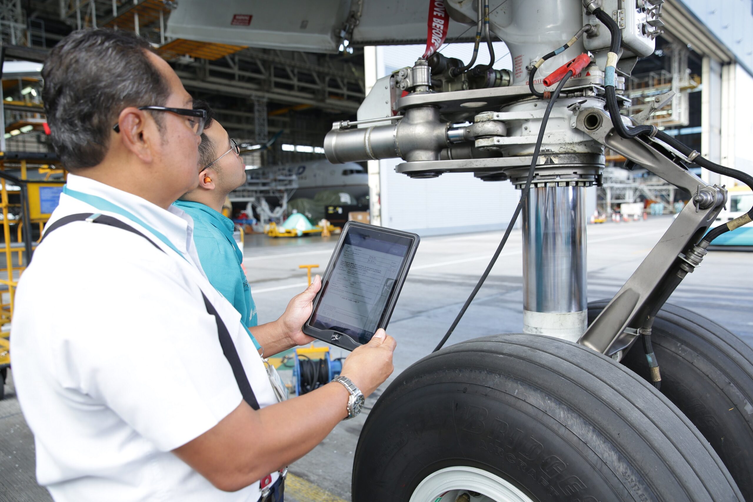 HAECO technicians consult a mobile electronic task card beside an aircraft landing gear assembly