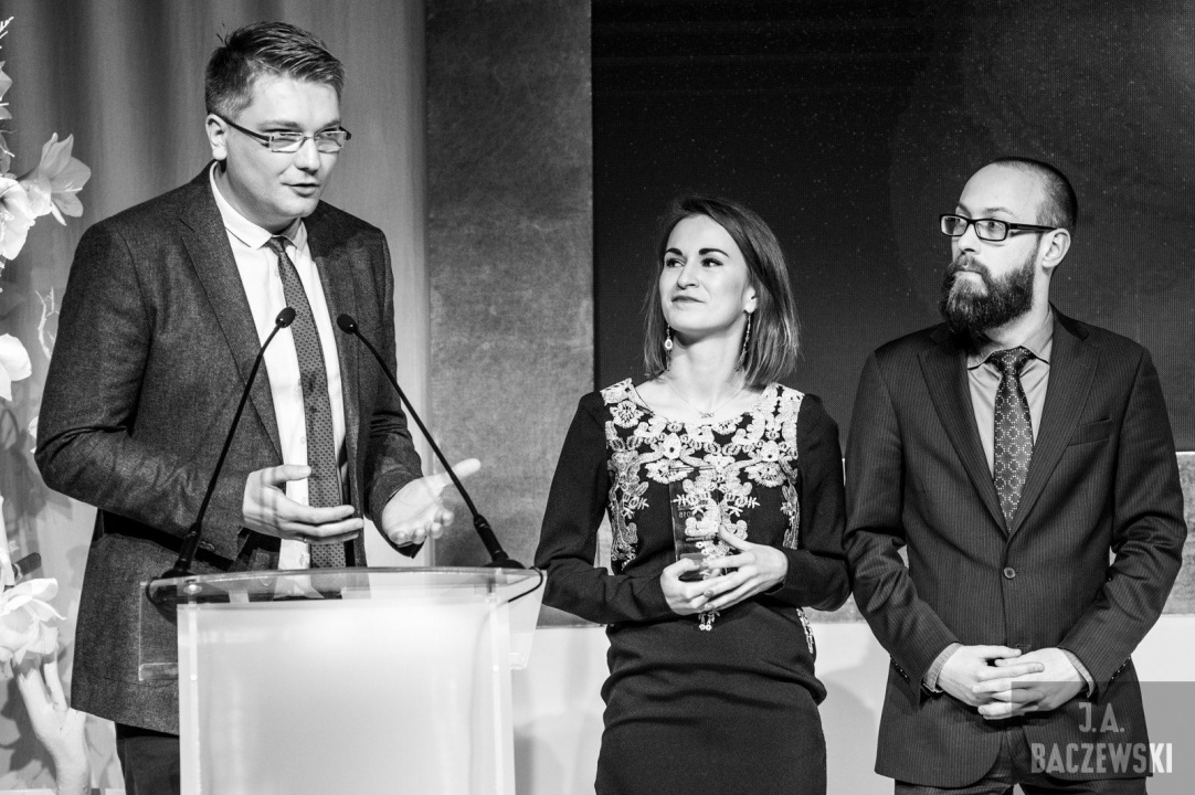 Three representatives stand onstage with a Złote Spinacze award in 2015