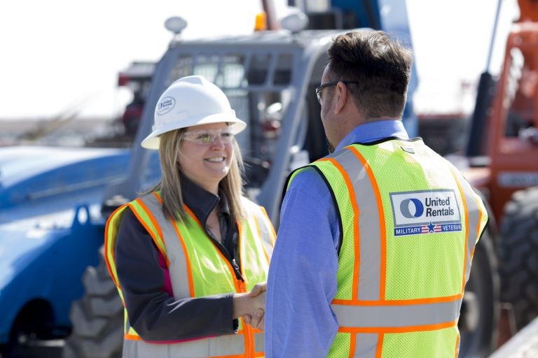Two United Rentals employees in high visibility safety clothing beside equipment