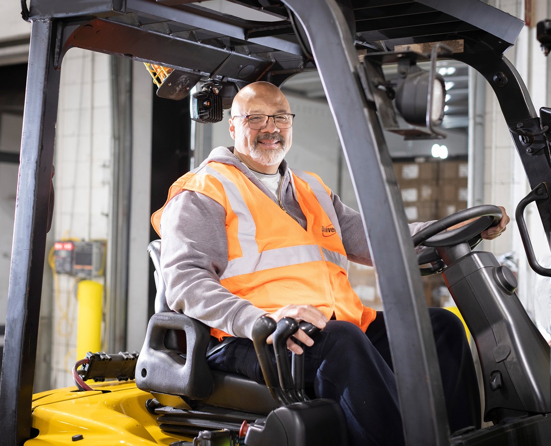 A smiling forklift operator wearing an orange safety vest at a Universal facility