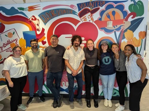 Eight Unqork team members standing together in front of a colourful volunteer mural