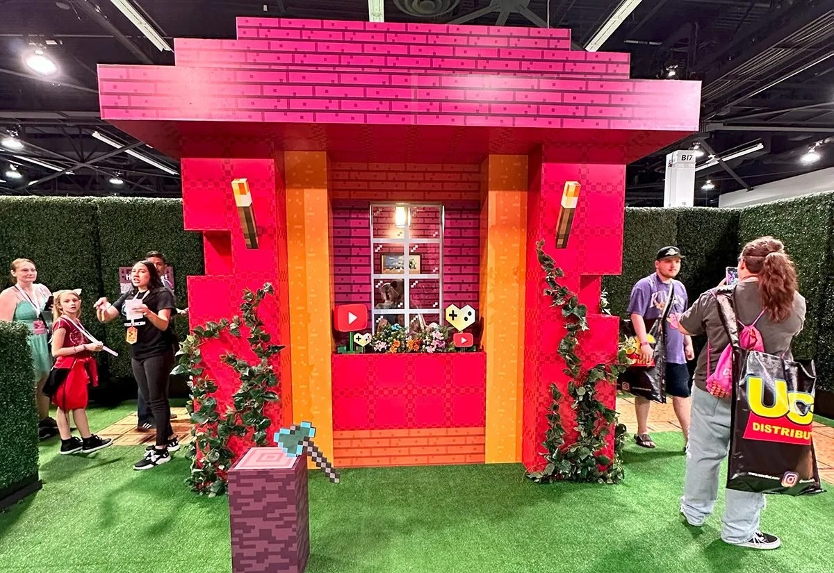 Visitors gather beside a bright pink and orange Minecraft-style house at VidCon 2024