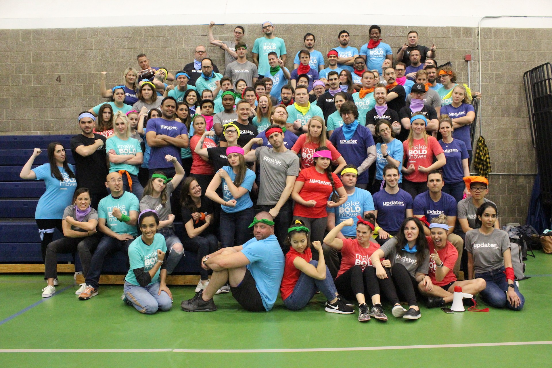 Historical Updater team photograph with colleagues in company shirts posing on gym bleachers