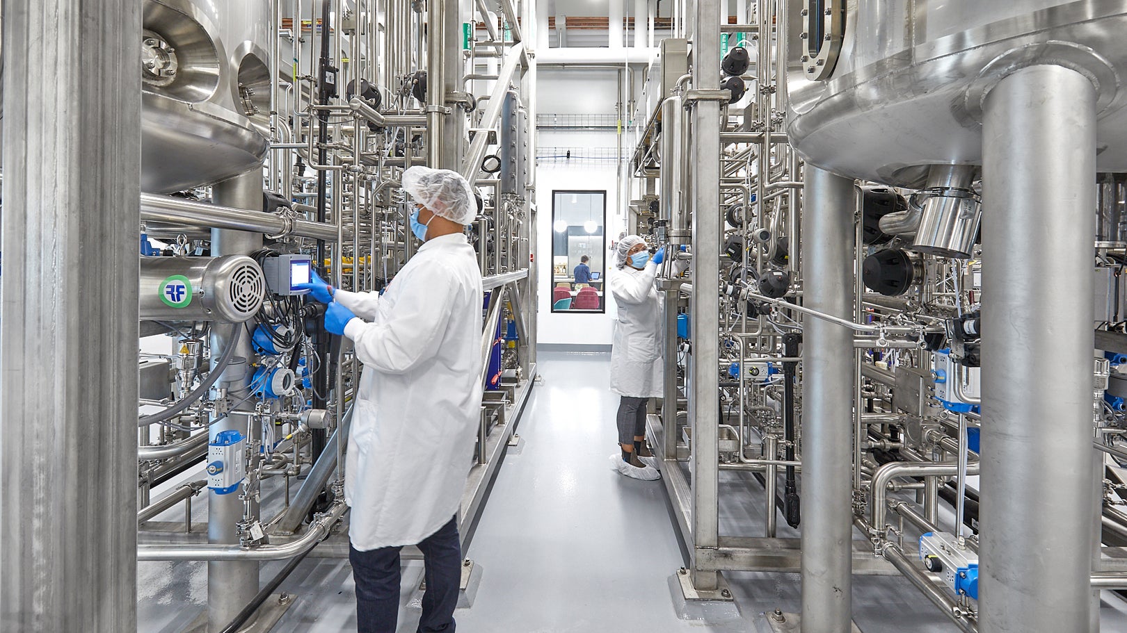 Workers in lab coats and hairnets inside UPSIDE Foods' EPIC production facility, surrounded by stainless-steel bioreactors and piping