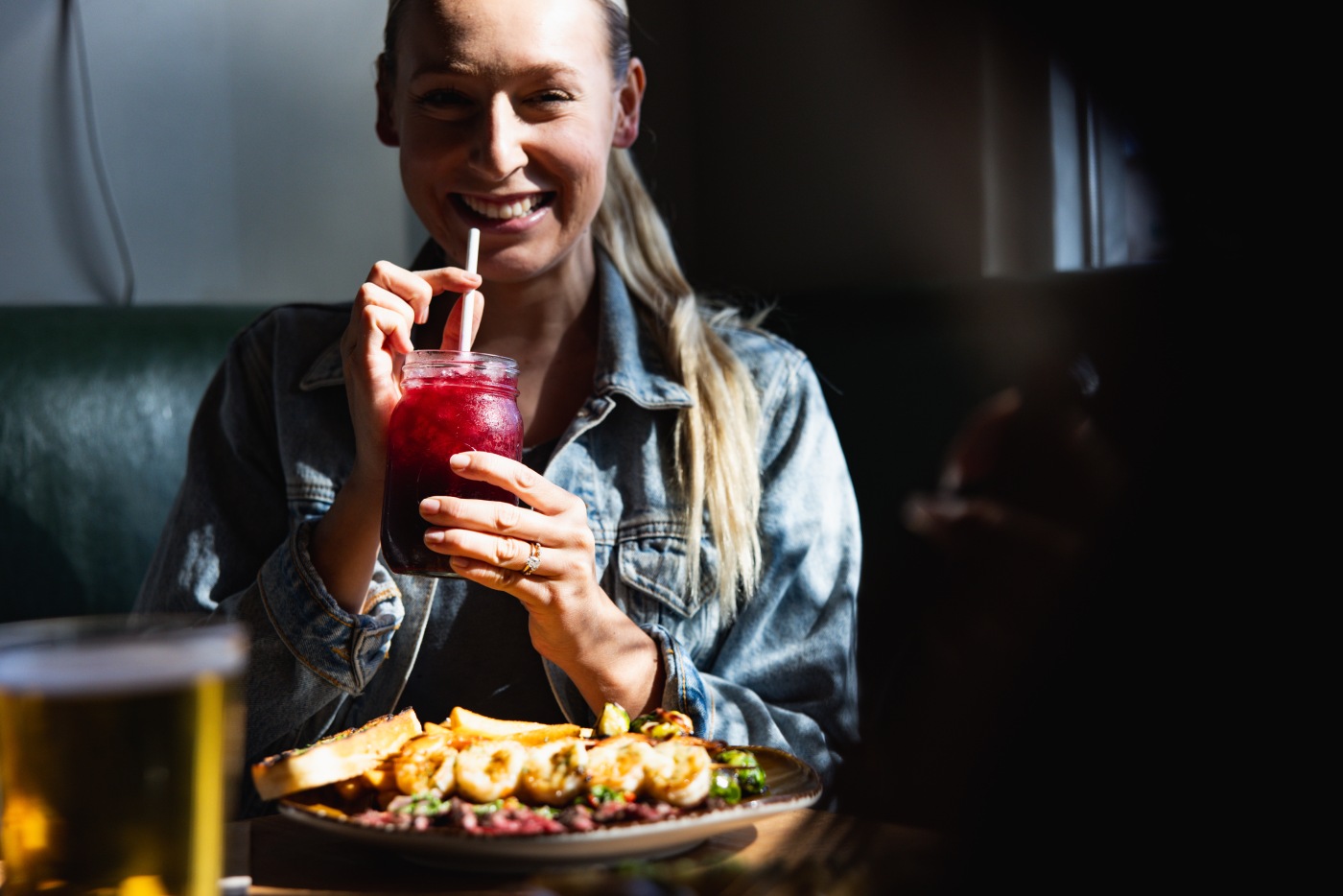 A diner holds a bright red drink beside a plate of food at Urban Plates