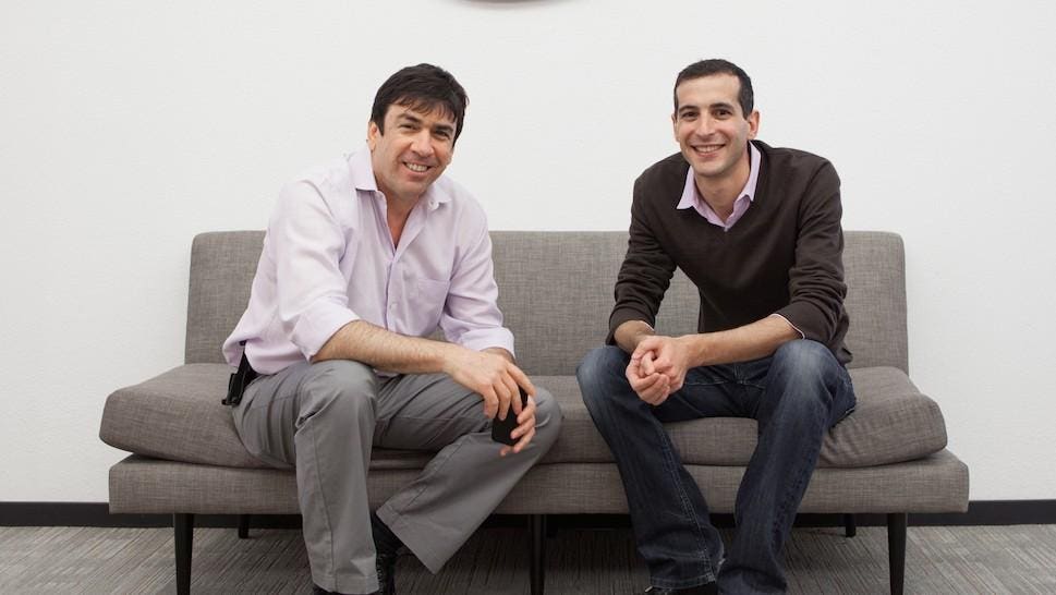 Uri Raz and Eric Setton seated together on a gray sofa