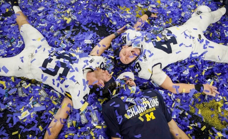 Michigan football players celebrate lying in a field of blue and yellow championship confetti