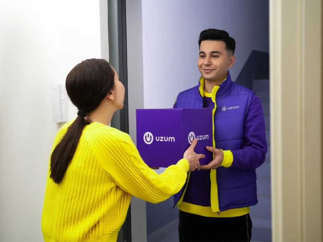 A Uzum employee hands a purple parcel to a customer