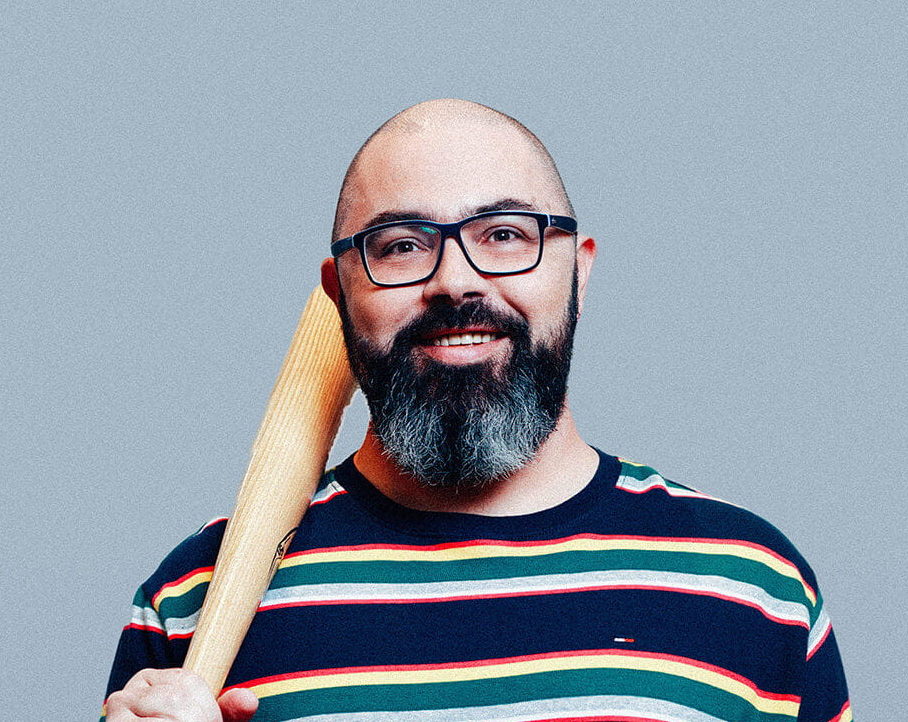 Vadim Solovey smiling in glasses and a striped shirt, with a wooden bat resting on his shoulder