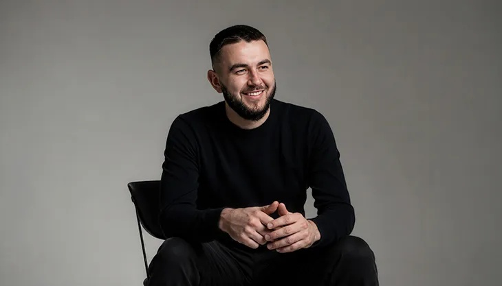 Val Pavliuchenko seated on a chair, smiling with his hands clasped