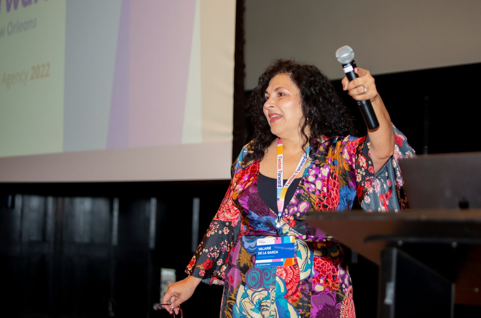 Valarie de la Garza holding a microphone while addressing colleagues at Fenton Forward in New Orleans