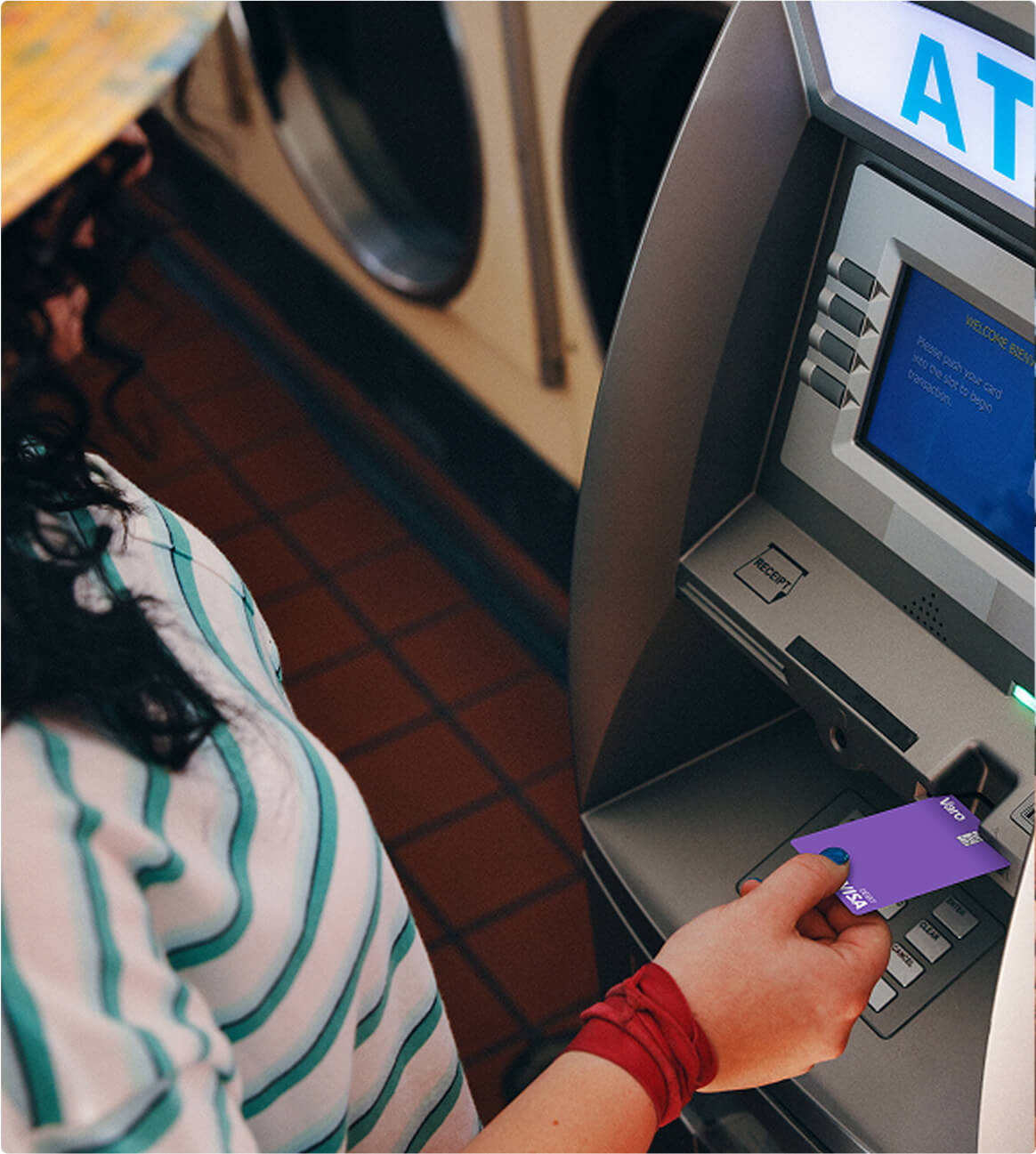 A customer holding a purple Varo debit card beside an ATM
