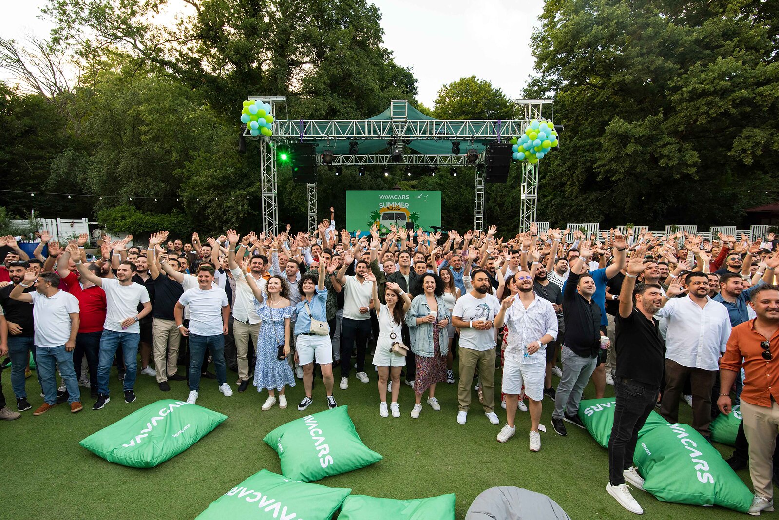 VavaCars employees waving at an outdoor summer gathering with green branded cushions