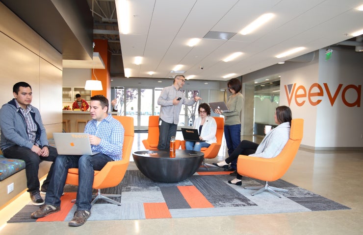 Veeva colleagues working and talking in an office lounge with orange chairs.