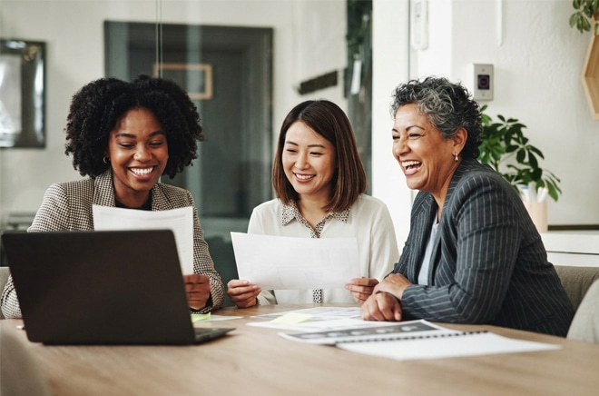 Three school professionals reviewing documents around a laptop